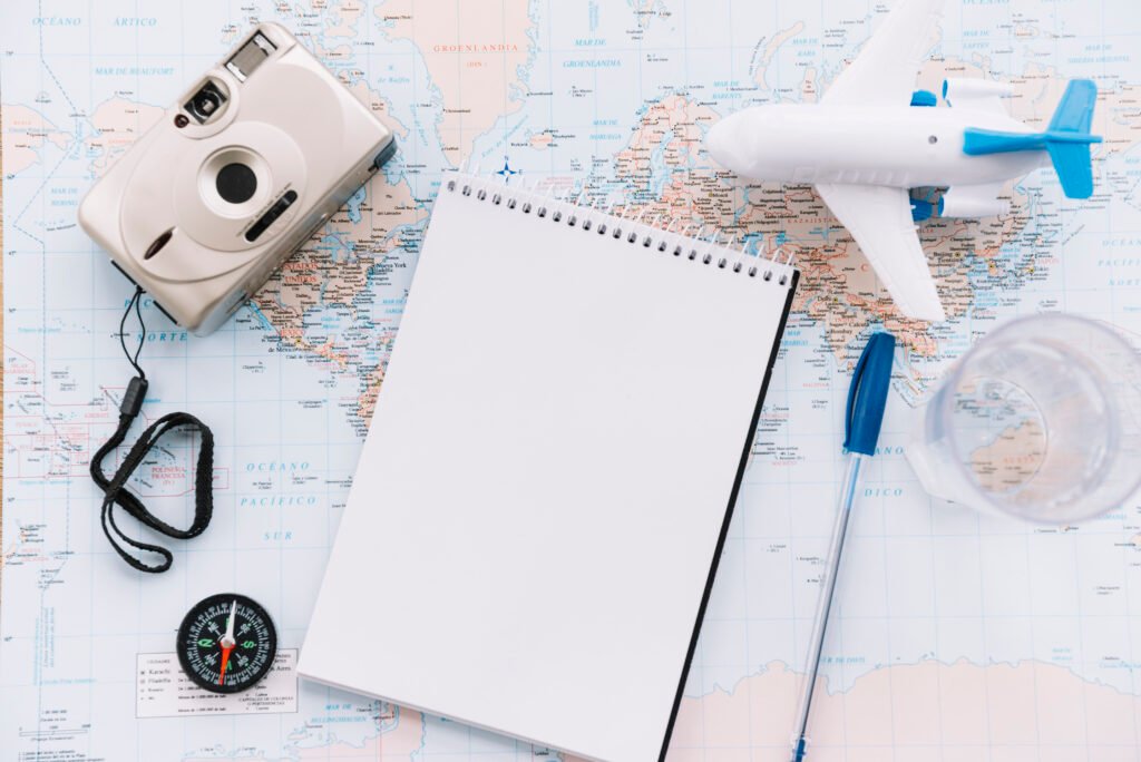 overhead view miniature white airplane spiral blank notepad pen camera compass map