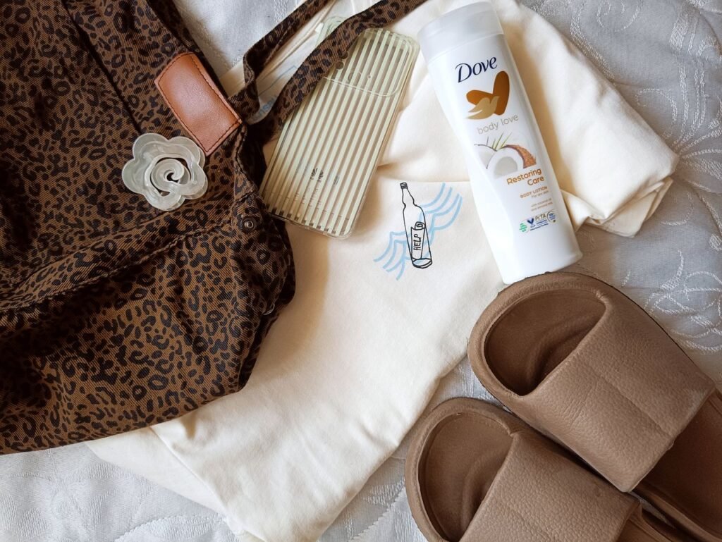 Flat lay of leopard print bag, Dove body lotion, sandals, and accessories on bed.