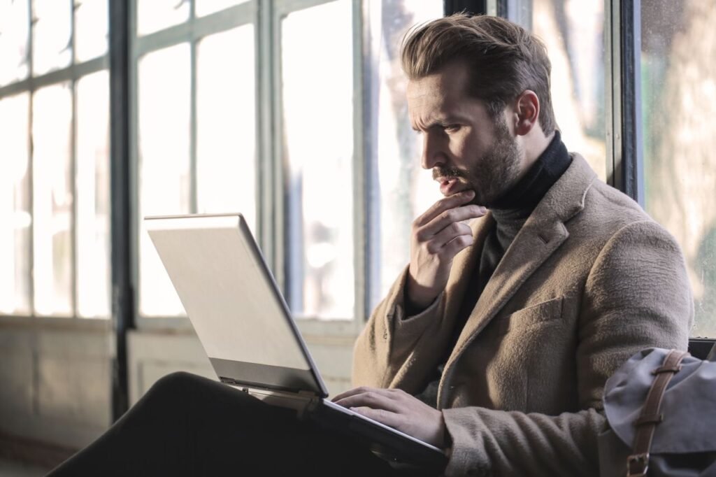 Best Time to Book Flights for Maximum Savings Man looking contemplative while working on a laptop in a well-lit indoor space.